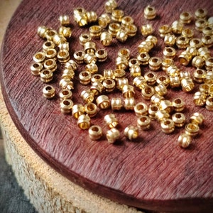 May include: A close-up of a pile of gold-colored metal beads on a wooden surface. The beads are small and round, with a slightly textured surface.
