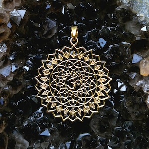 Puede incluir: Un colgante dorado con un diseño de mandala detallado con un símbolo Om en el centro. El colgante está hecho de metal y tiene un estilo de filigrana.