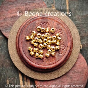 Peut inclure: Gros plan sur un tas de perles en métal de couleur dorée. Les perles sont rondes avec un petit trou au centre. Les perles sont sur une surface en bois.