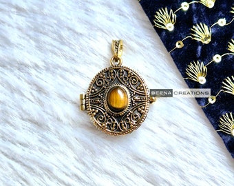 May include: A gold locket pendant with an ornate design and a tiger's eye stone in the center. The locket is open and the inside is visible.