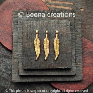 Puede incluir: Cuatro abalorios de plumas de color dorado con un bucle en la parte superior para sujetar a joyas u otras manualidades.