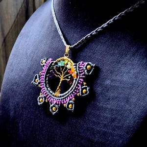 May include: A gray cord necklace with a purple and gray macrame pendant featuring a gold wire tree of life with colorful gemstones.