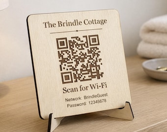May include: A wooden Wi-Fi sign with the text "The Brindle Cottage" and a QR code. Below the QR code, it reads "Scan for Wi-Fi", network name, and password. The sign is displayed on a wooden stand.