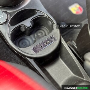 May include: A close-up of a car's interior with two cup holders and a USB port. The cup holders and the surrounding area are covered in a black glitter material. The text "Black Glitter" is visible in the image.
