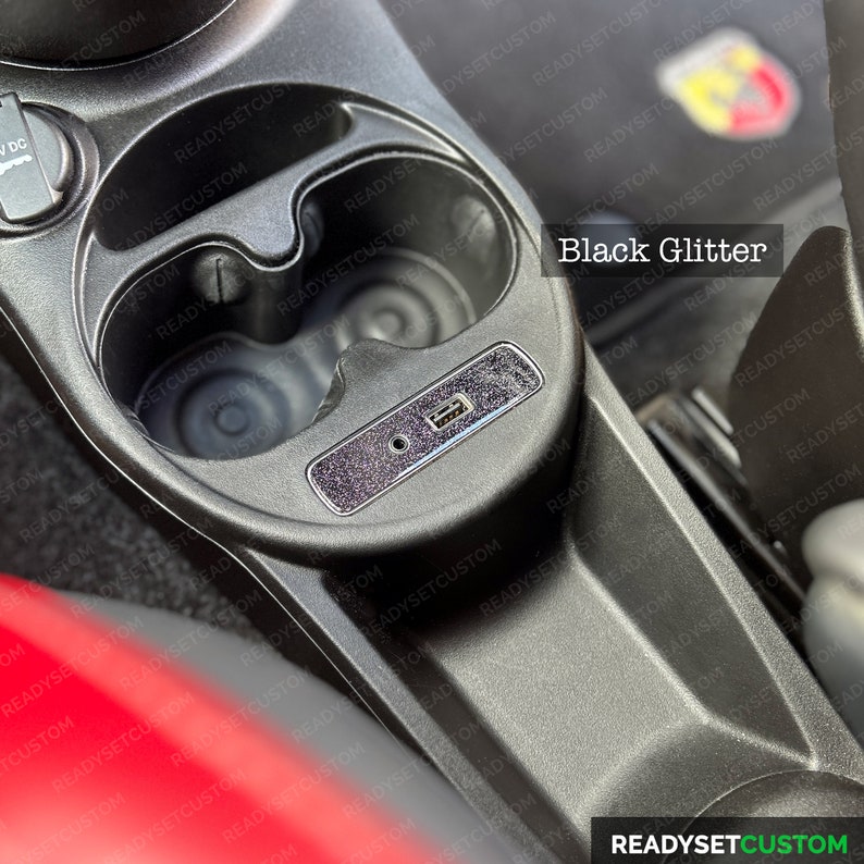May include: A close-up of a car's interior with two cup holders and a USB port. The cup holders and the surrounding area are covered in a black glitter material. The text "Black Glitter" is visible in the image.