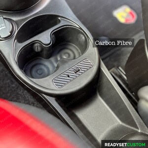May include: A close-up of a car's interior with two cup holders and a carbon fiber trim piece. The trim piece has a USB port and the text "Carbon Fibre" is visible.