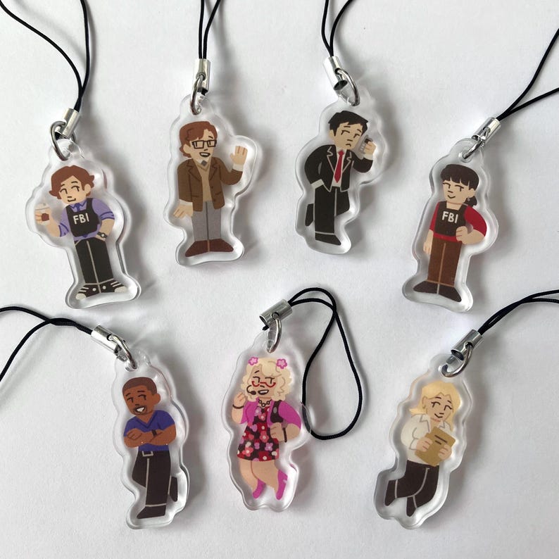 May include: A collection of seven clear acrylic charms featuring cartoon illustrations of characters. Each charm has a black lanyard attached. The characters are dressed in various outfits, with some displaying the "FBI" logo.