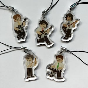 May include: Set of five clear acrylic charms featuring cartoon musicians playing instruments. Each charm depicts a musician in a white shirt and brown pants, with a guitar, keyboard, or drumsticks. Black cords and silver clasps are attached.