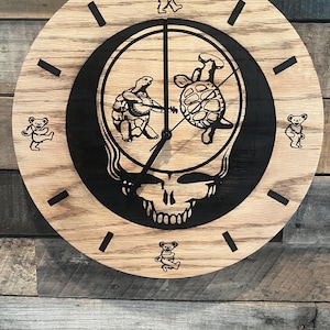 May include: A round wooden clock with a black skull and turtle design in the center. The clock face has black markers and dancing bear figures. The clock hands are black.