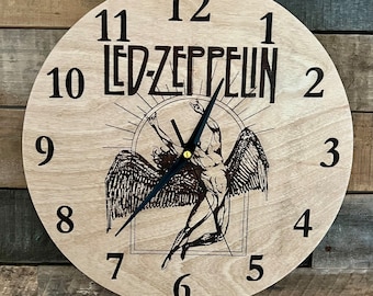 Könnte beinhalten: Eine runde Holzuhr mit dem Led Zeppelin-Logo und einer Schwarz-Weiß-Illustration einer geflügelten Figur. Die Uhr hat schwarze Ziffern und Zeiger. Die Uhr ist aus hellfarbenem Holz gefertigt.