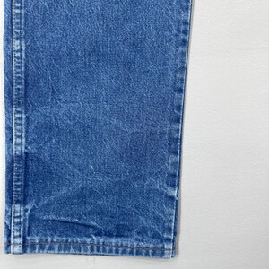 Pode incluir: Close-up de uma se&ccedil;&atilde;o de jeans azul. Os jeans t&ecirc;m um design cl&aacute;ssico de cinco bolsos com costuras vis&iacute;veis e uma lavagem desbotada. A imagem mostra a bainha e a costura lateral dos jeans.
