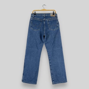 May include: A pair of blue denim jeans hanging on a wooden hanger. The jeans have a classic straight leg style and a light wash.