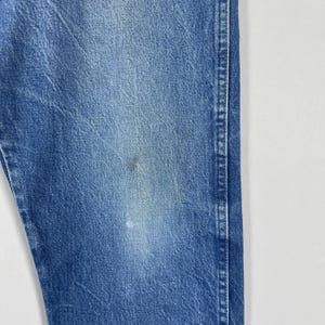 Pode incluir: Close-up de uma se&ccedil;&atilde;o de jeans azul. O tecido mostra desgaste e desbotamento, com uma mancha mais escura e uma mancha mais clara. Os jeans t&ecirc;m um estilo cl&aacute;ssico e casual.