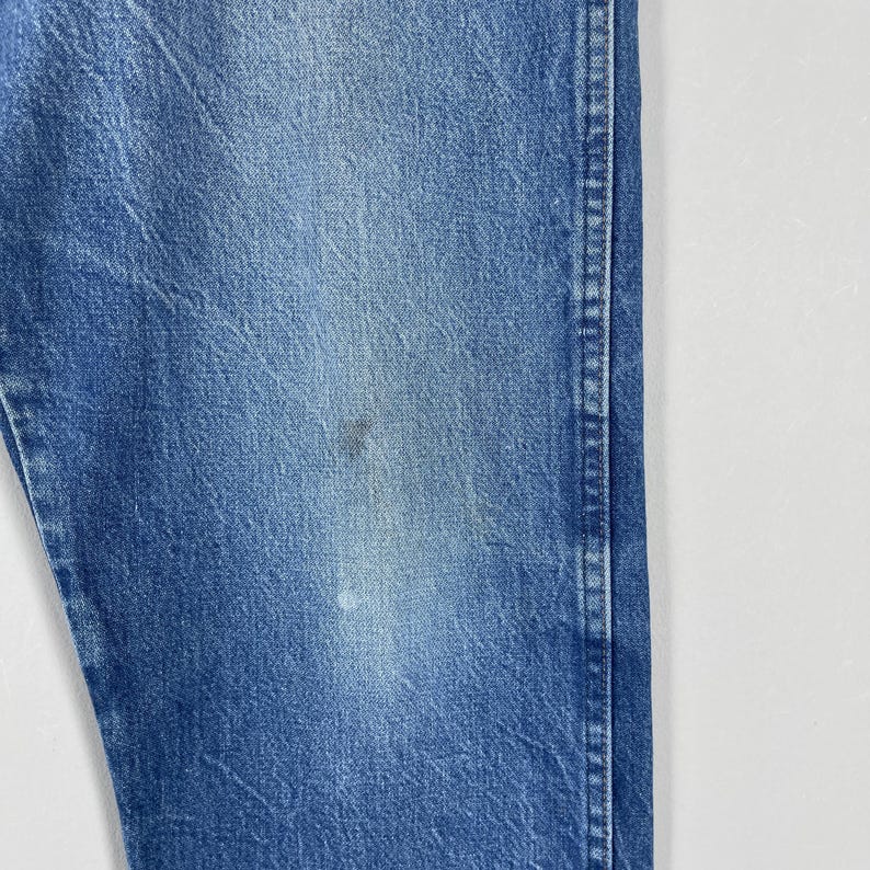 Pode incluir: Close-up de uma se&ccedil;&atilde;o de jeans azul. O tecido mostra desgaste e desbotamento, com uma mancha mais escura e uma mancha mais clara. Os jeans t&ecirc;m um estilo cl&aacute;ssico e casual.