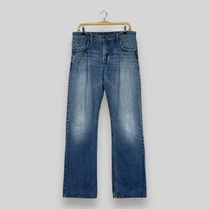 May include: A pair of blue denim jeans hanging on a wooden hanger. The jeans have a straight leg and a classic five-pocket design.