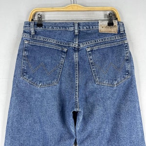 May include: A pair of blue denim jeans with a back pocket featuring a stitched 'W' logo and a brown leather patch with the text 'Wrangler' in white.