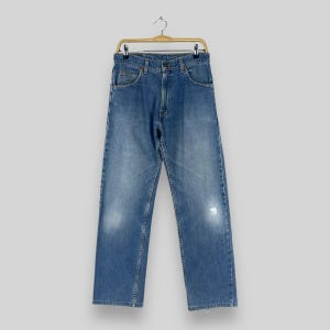 Puede incluir: Un par de pantalones vaqueros azules colgados de una percha. Los vaqueros tienen un aspecto descolorido y un pequeño agujero en la pierna derecha.