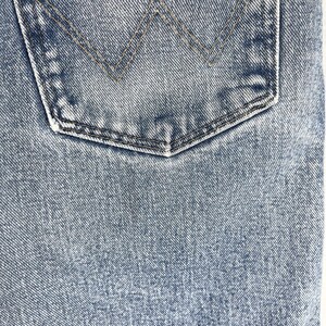 May include: Close-up of a blue denim fabric with a back pocket. The pocket has a stitched detail in the shape of a triangle.