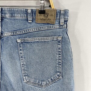Może przedstawiać: Dżinsy w kolorze niebieskim z tylną kieszenią i brązową sk&oacute;rzaną naszywką z napisem "Wrangler Authentic Jeans".