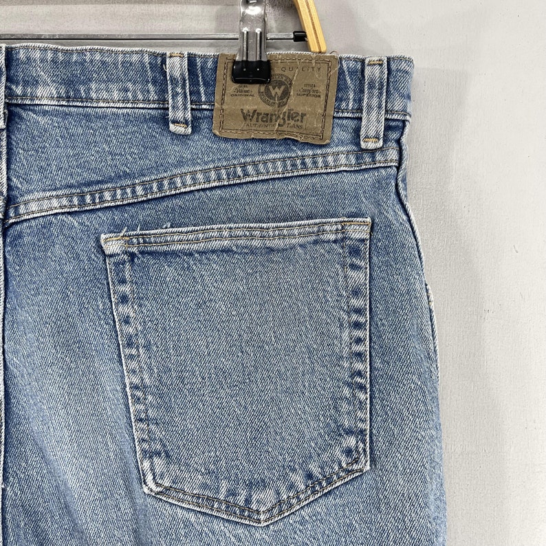 Może przedstawiać: Dżinsy w kolorze niebieskim z tylną kieszenią i brązową sk&oacute;rzaną naszywką z napisem "Wrangler Authentic Jeans".