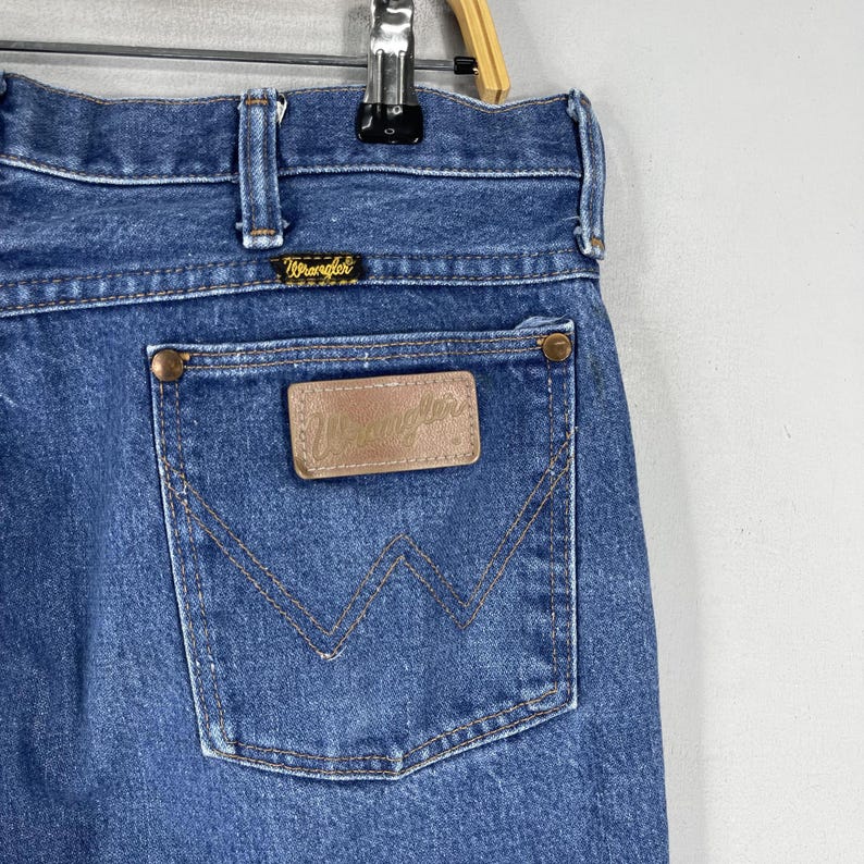 May include: A pair of blue denim jeans with a brown leather patch that says "Wrangler" on the back pocket.