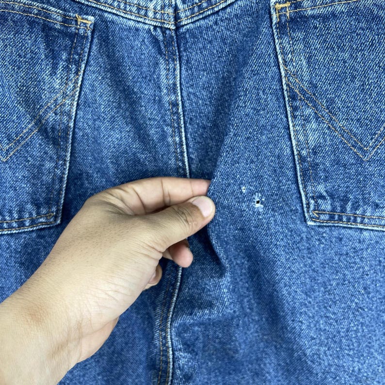 K&ouml;nnte beinhalten: Nahaufnahme einer blauen Jeanshose mit einem kleinen Loch im Stoff.