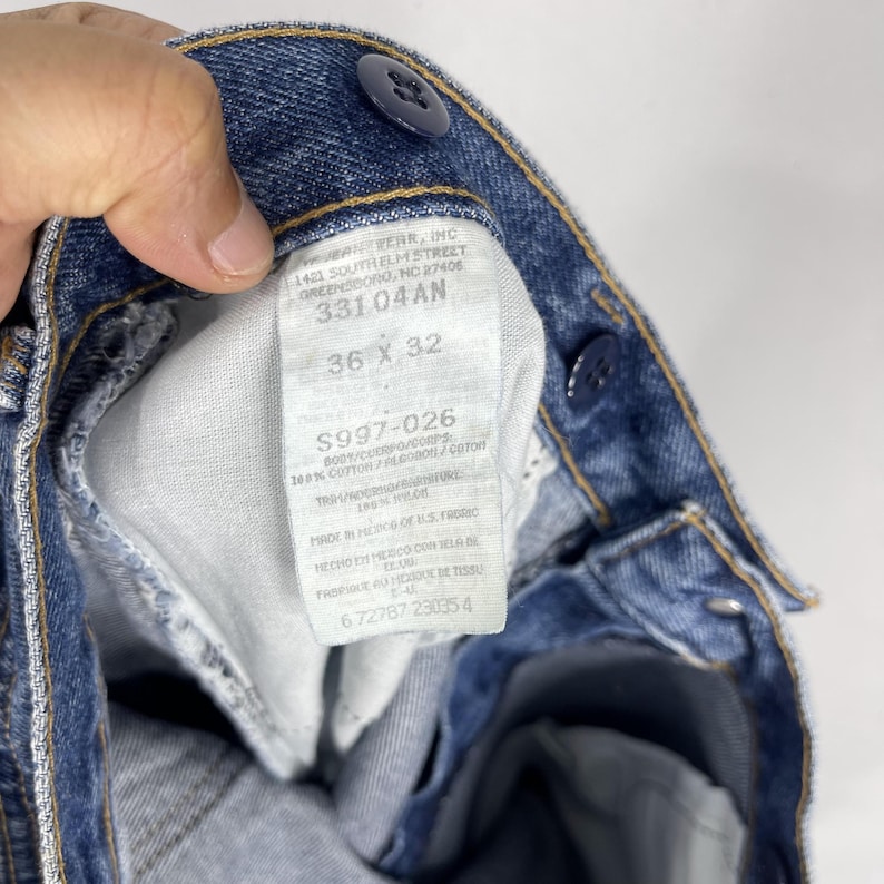 K&ouml;nnte beinhalten: Nahaufnahme eines blauen Jeans-Etiketts mit dem Text "1421 SOUTHELM STREET GREENSBORO, NC 27408 33104AN 36 X 32 $997-026 B001/CLEPO/CORPS 100% COTTON/ALGODON/COTON 100% COTTON/ALGODON/COTON MADE IN MEXICO OF U.S. FABRIC HECHO EN MEXICO CON TELA DE EE.UU.  PRODUIT EN MEXIQUE DE TISSU 6 72787 230354"