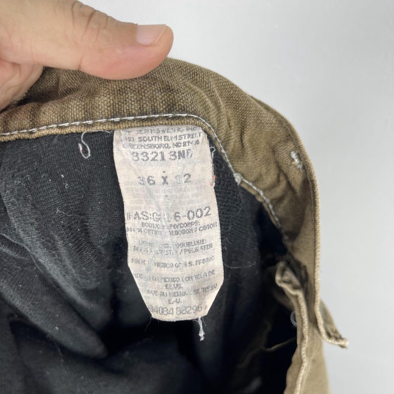 May include: Close-up of the inside of a pair of brown work pants. The tag reads "36 x 32" and includes other text. The pants are made of a durable material, with a black lining. The stitching is visible.