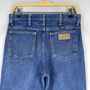 K&ouml;nnte beinhalten: Eine blaue Jeanshose mit einem braunen Leder-Patch auf der Ges&auml;&szlig;tasche, auf dem "Wrangler" steht.