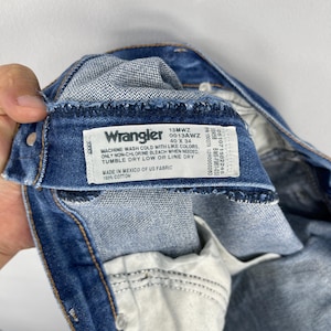 Pode incluir: Close-up do interior de um par de jeans Wrangler azuis. A etiqueta dos jeans &eacute; vis&iacute;vel, exibindo a marca, o tamanho 40 x 34 e as instru&ccedil;&otilde;es de cuidado. A etiqueta tamb&eacute;m informa que os jeans s&atilde;o feitos no M&eacute;xico com tecido dos EUA, 100% algod&atilde;o.