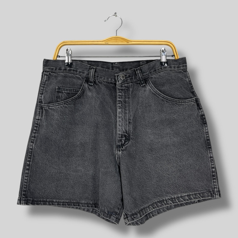Pode incluir: Um par de cal&ccedil;&otilde;es de ganga pretos pendurados num cabide de madeira. Os cal&ccedil;&otilde;es t&ecirc;m um design cl&aacute;ssico de cinco bolsos, fecho de bot&atilde;o e fecho de correr. A ganga tem um aspeto desbotado e gasto.