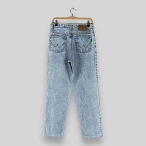 Pode incluir: Jeans de denim azul claro com lavagem desbotada e um remendo de couro marrom nas costas. As cal&ccedil;as jeans t&ecirc;m um caimento relaxado e uma perna reta.