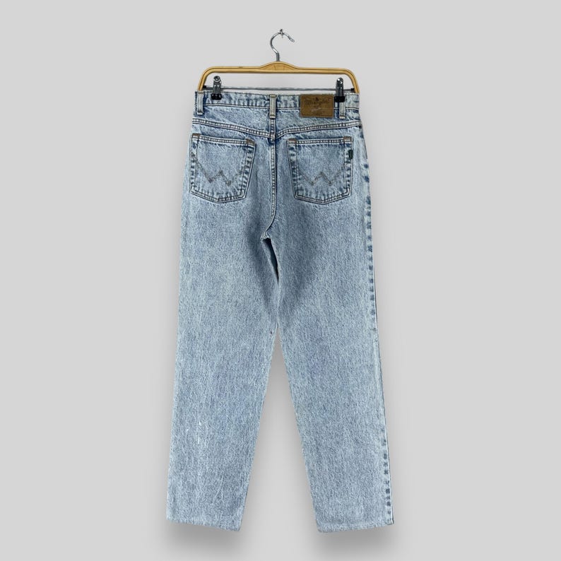 Pode incluir: Jeans de denim azul claro com lavagem desbotada e um remendo de couro marrom nas costas. As cal&ccedil;as jeans t&ecirc;m um caimento relaxado e uma perna reta.