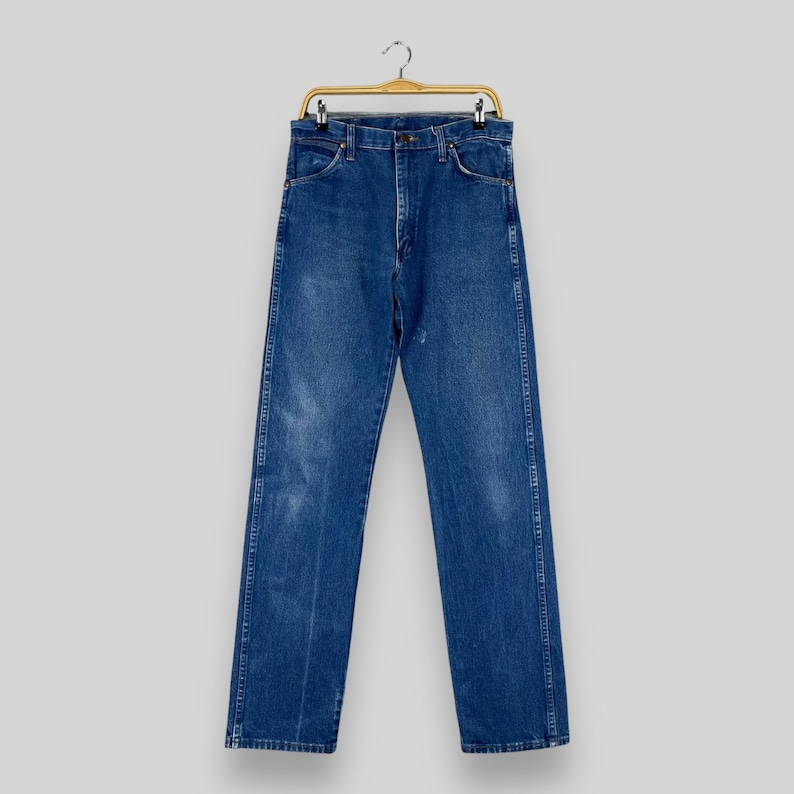 May include: A pair of blue denim jeans hanging on a wooden hanger. The jeans have a classic straight leg style and are made of a durable cotton blend.