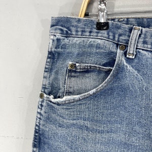 May include: Close-up of a light blue denim jean pocket with a button closure. The pocket is on a pair of jeans with a faded, distressed look.