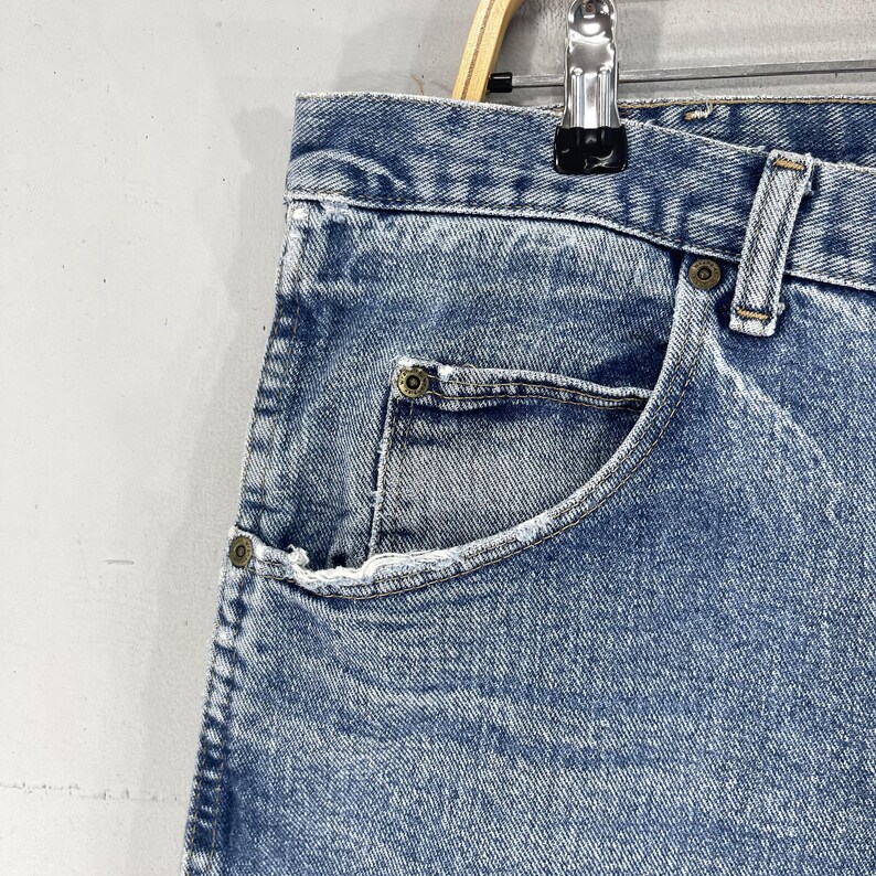 May include: Close-up of a light blue denim jean pocket with a button closure. The pocket is on a pair of jeans with a faded, distressed look.