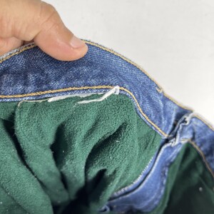 May include: Close-up of the inside of a pair of blue denim jeans. The jeans have a green fleece lining.