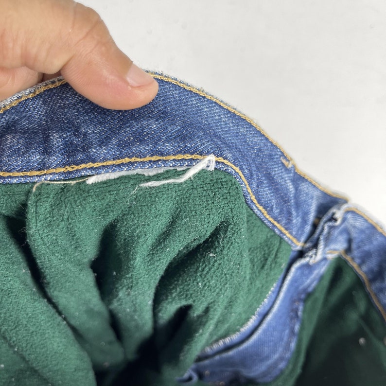 May include: Close-up of the inside of a pair of blue denim jeans. The jeans have a green fleece lining.