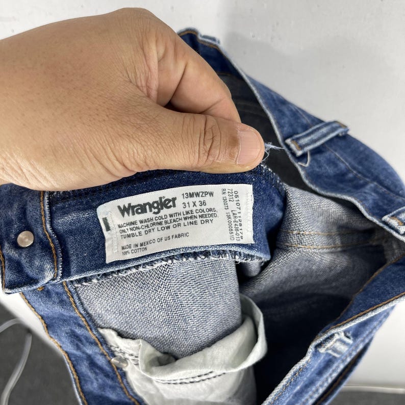 May include: Blue denim jeans with a Wrangler label that reads "13MWZPW 31 X 36" and includes care instructions. The label is attached to the inside of the waistband.