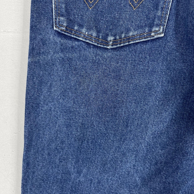 K&ouml;nnte beinhalten: Nahaufnahme von blauem Jeansstoff mit einer einzigen Ges&auml;&szlig;tasche. Die Tasche hat einen gen&auml;hten Rand und eine dezente, ausgewaschene Optik.