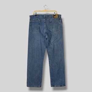 May include: Light blue denim jeans hanging on a wooden hanger. The jeans have a classic five-pocket design, with a leather patch on the back. The jeans are a medium wash and appear to be in good condition.