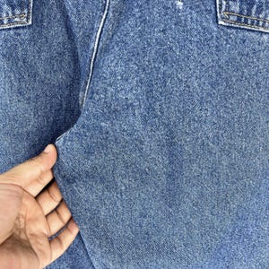 K&ouml;nnte beinhalten: Nahaufnahme von blauem Jeansstoff mit einer strukturierten Webart. Der Stoff ist gefaltet und zeigt die N&auml;hte entlang der Naht.