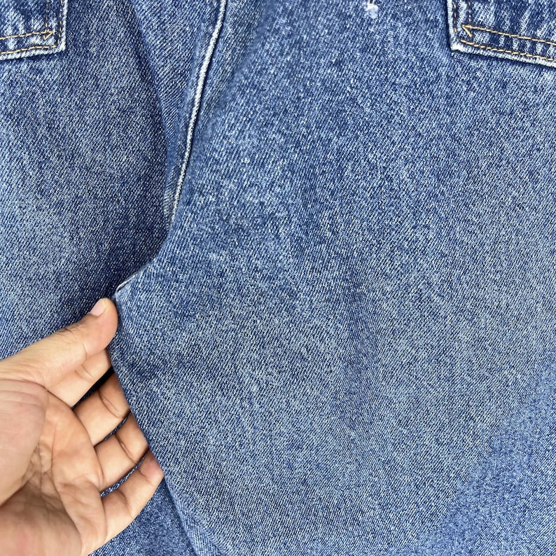 K&ouml;nnte beinhalten: Nahaufnahme von blauem Jeansstoff mit einer strukturierten Webart. Der Stoff ist gefaltet und zeigt die N&auml;hte entlang der Naht.