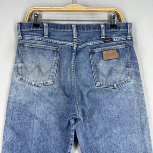 May include: A pair of blue denim jeans with a brown leather patch on the back pocket that says "Wrangler".