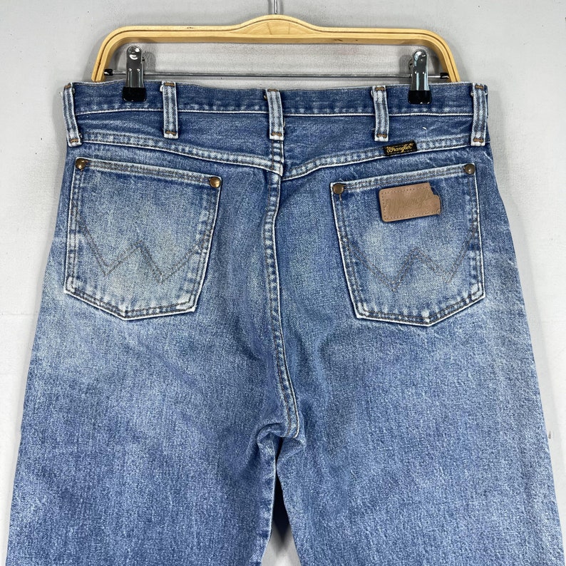May include: A pair of blue denim jeans with a brown leather patch on the back pocket that says "Wrangler".