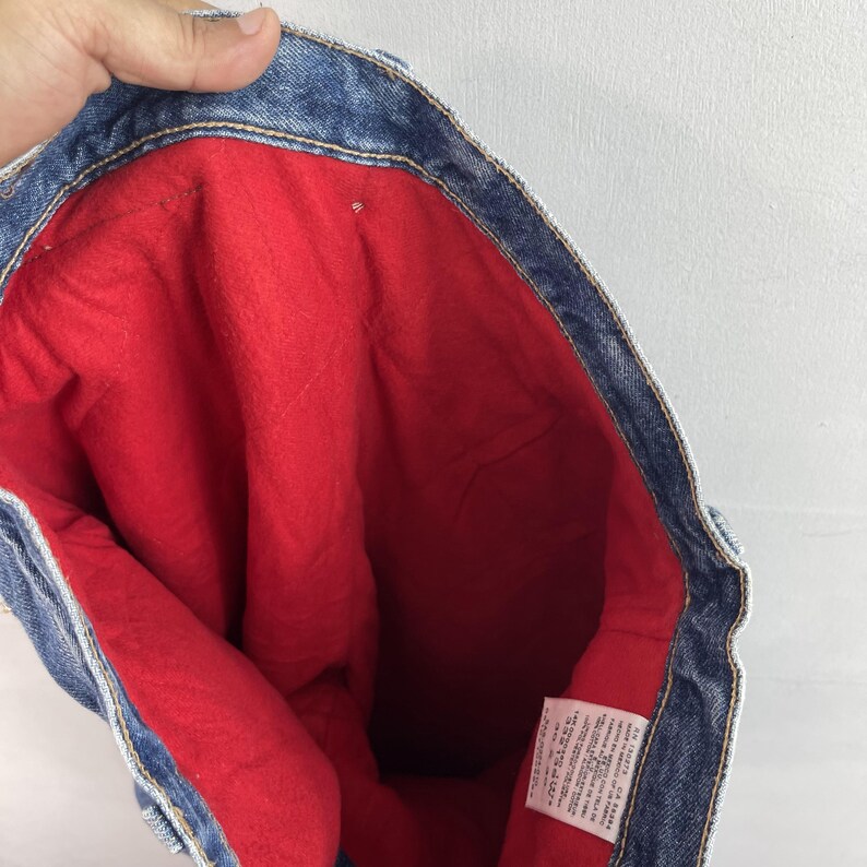 May include: Inside of a pair of blue denim jeans with a red fleece lining. The jeans have a care label with washing instructions.