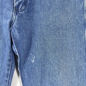 May include: Close-up of blue denim fabric with a faded, distressed look. The fabric has a subtle texture and a light blue color.