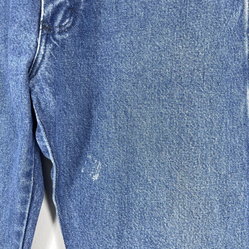 May include: Close-up of blue denim fabric with a faded, distressed look. The fabric has a subtle texture and a light blue color.
