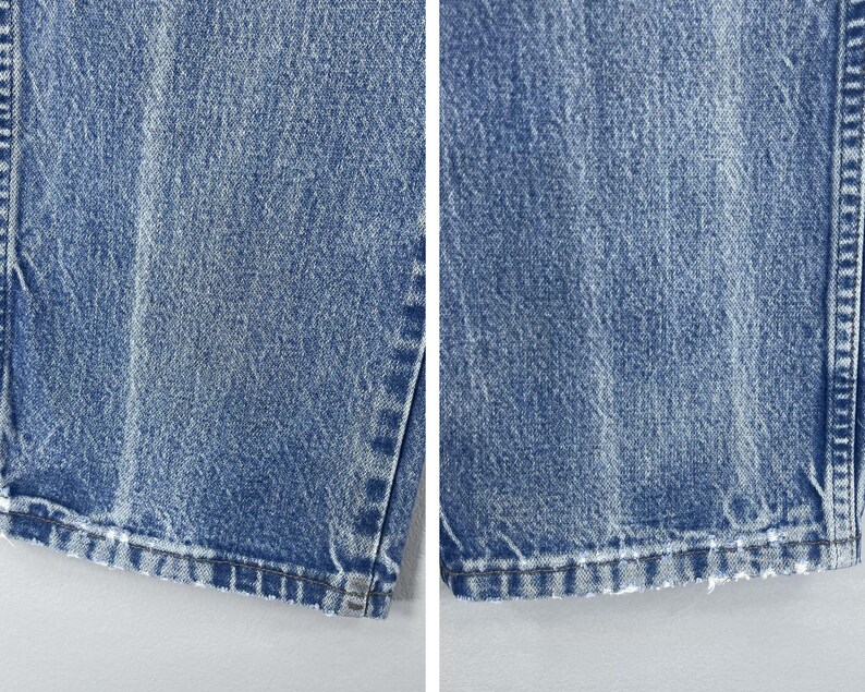 Pu&ograve; includere: Primo piano del bordo inferiore di un paio di jeans blu chiaro. I jeans hanno un aspetto consumato e sono sfilacciati sul bordo.