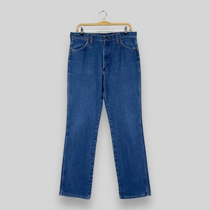 May include: A pair of blue denim jeans hanging on a wooden hanger. The jeans have a classic straight leg style and a button fly.
